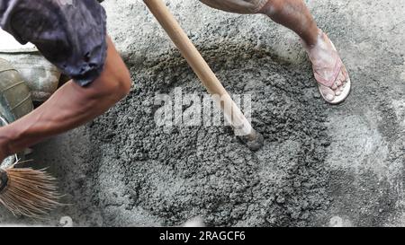 Travailleur asiatique utilisant la houe pour mélanger la puissance du ciment avec le sable Banque D'Images