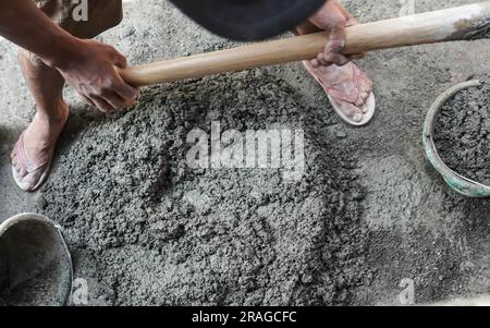 Travailleur asiatique utilisant la houe pour mélanger la puissance du ciment avec le sable Banque D'Images