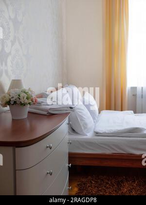 Design intérieur dans des couleurs claires. Lit et commode avec serviettes et fleurs dessus, foyer sélectif Banque D'Images
