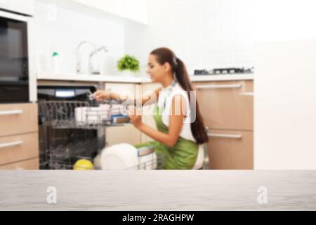 Une jeune femme charge le lave-vaisselle dans la cuisine, se concentre sur une table vide Banque D'Images