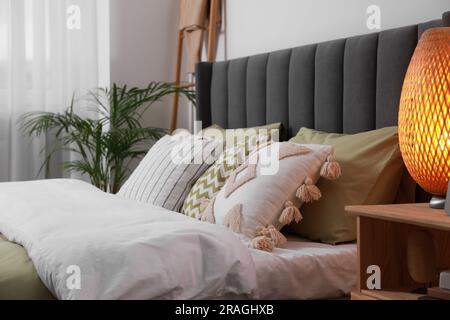 Lit confortable avec coussins, lampe sur table de chevet en bois dans la chambre. Intérieur élégant Banque D'Images