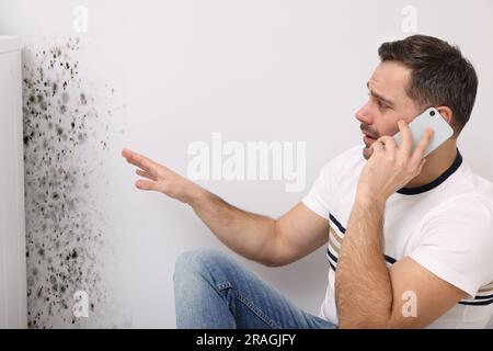 Service de dépose du moule. Homme parlant au téléphone et regardant le mur affecté dans la chambre Banque D'Images