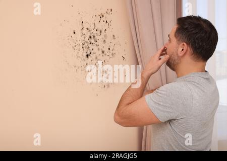 Homme choqué regardant affecté avec le mur de moule dans la chambre Banque D'Images