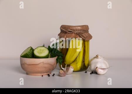 Délicieux concombres marinés, couper les légumes dans un bol en bois et l'ail sur une table blanche Banque D'Images