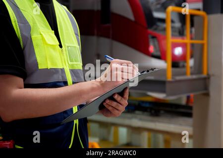 Gros plan mains de l'ingénieur homme ou de l'ouvrier vérifiant le train électrique pour la planification de la maintenance et écrire le document sur le presse-papiers dans la gare, le transport et moi Banque D'Images