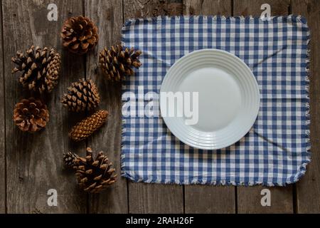 Assiette blanche sur une serviette en cage sur une table en bois et à côté des cônes d'un arbre de Noël, décoration de table du nouvel an Banque D'Images