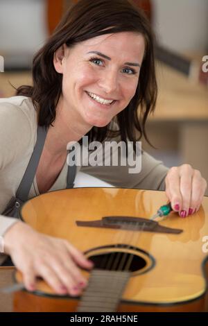 la femme luthier met une guitare au diapason de son atelier d'instruments Banque D'Images