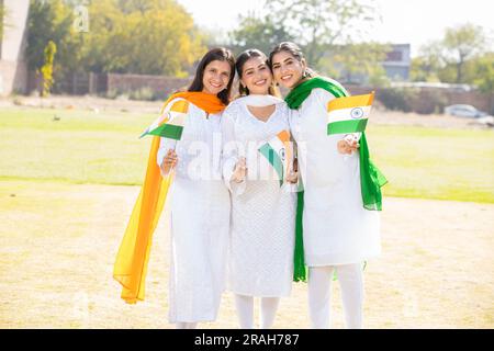 Trois jeunes belles femmes portant la robe blanche traditionnelle tenant le drapeau indien tout en .debout au parc ensemble célébrant le jour de l'indépendance ou Repub Banque D'Images