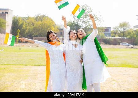 Trois jeunes belles filles portant une robe blanche traditionnelle tenant le drapeau indien tout en .debout au parc ensemble ayant du plaisir à célébrer l'indépendance d Banque D'Images