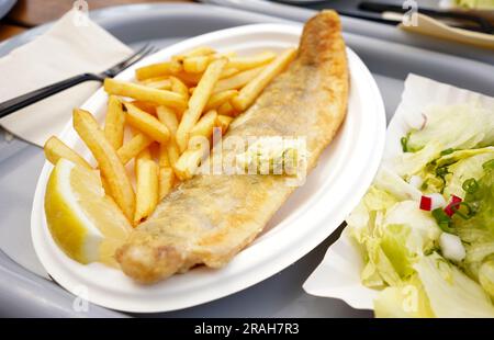 Fish and chips sur une assiette. Poisson frit avec du beurre dessus et frites sur une assiette en plastique dans le restaurant Banque D'Images