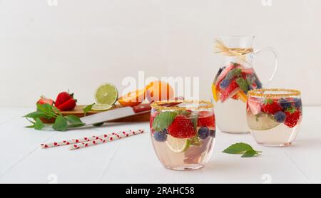 Deux verres bas et un pichet remplis d'eau aromatisée aux fruits et de tranches de fruits, avec planche à découper affichant une gamme d'orange fraîche, de fraise, de li Banque D'Images