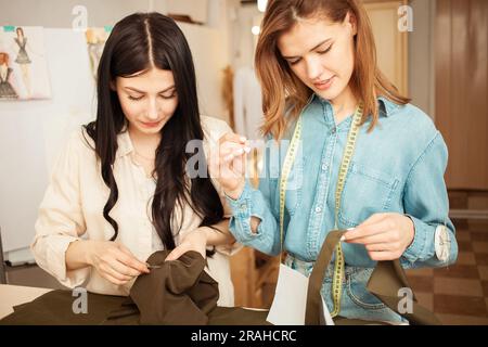 Les couturières cousent le tissu à la main, balayent les détails de la future tenue. Processus de travail, artisanat, lieu de travail. cheveux noirs et cheveux roux Banque D'Images