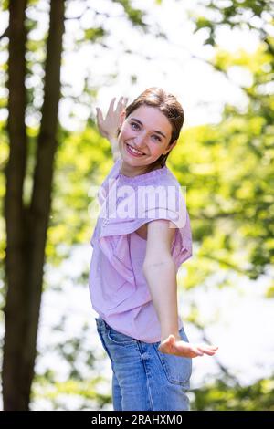 Vivez le bonheur pur et la joie rayonnante alors qu'une jeune femme se tient au milieu d'une journée d'été baignée de soleil, les bras grands ouverts, embrassant la chaleur de la nature dans la forêt enchanteresse. Cette photo vue de côté capture son esprit insouciant alors qu'elle s'immerge dans la verdure vibrante, debout entre les arbres majestueux. La lumière du soleil dorée filtre à travers les feuilles, jetant une belle lueur sur elle alors qu'elle se délecte de la tranquillité et de la beauté du monde naturel. Témoin de son expression de pur bonheur comme elle se prélasse dans la sérénité et la liberté que seule la forêt peut offrir., embrassant Natur Banque D'Images