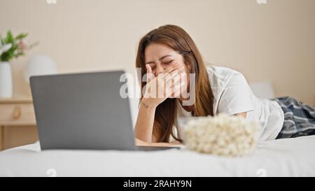 Jeune belle femme hispanique regardant un film humoristique couché sur le lit riant beaucoup à la chambre Banque D'Images