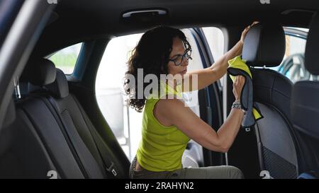 Femme hispanique d'âge moyen nettoyant l'intérieur de la voiture avec un chiffon en microfibre au poste de lavage de voiture Banque D'Images