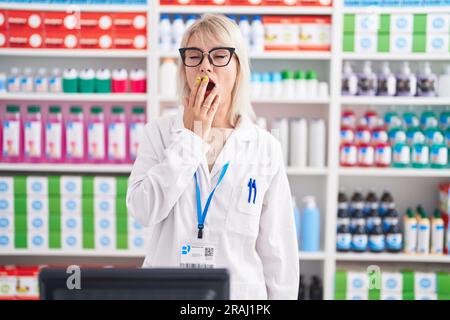 La jeune femme caucasienne travaillant à la pharmacie s'est ennuie bâilling fatiguée couvrant la bouche avec la main. Agité et somnolence. Banque D'Images