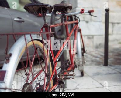 un vélo rouge, rare pour deux personnes, avec deux sièges, se dresse dans le parking à côté d'une voiture grise. Gros plan d'un vélo depuis l'arrière. Photo de haute qualité Banque D'Images