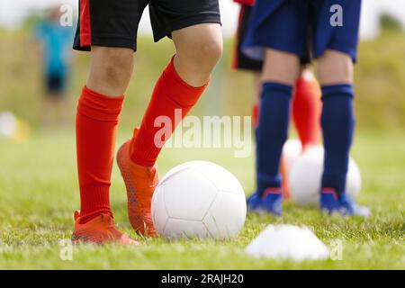 Joueurs de football Kicking Classic White Soccer Balls sur la session d'entraînement. Contexte du football des jeunes. Jeune garçon portant des crampons de football et des chaussettes de football. Banque D'Images