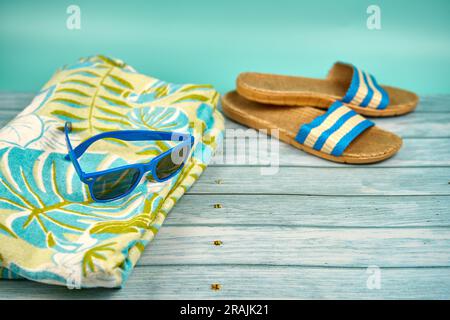 Lunettes de soleil bleues, sandales et serviette de plage, sur une table en bois et un fond vert. Banque D'Images