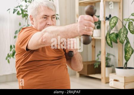 Vieux homme âgé dans la formation de sportswear dans la salle de séjour faire le poids lever haltères exercice à la maison, Loisirs vie saine. Un homme plus âgé est un homme qui travaille Banque D'Images