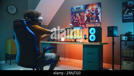 Adolescent afro-américain dans le casque VR joue au jeu de tir virtuel à la troisième personne 3D sur ordinateur personnel en utilisant des contrôleurs sans fil. Jeu vidéo en ligne streaming ou championnat de cybersport. Jeux à la maison. Banque D'Images