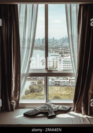 Coussin d'oiseau noir placé sur le coussin de siège à côté de la fenêtre. En regardant par la fenêtre de la chambre, vous pourrez admirer la magnifique vue sur la ville de Bangkok et Chao Phraya Banque D'Images