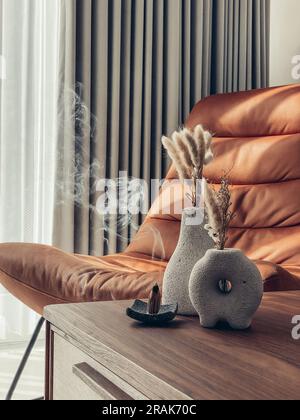 Vases décoratifs en pierre de lave avec fleurs sèches et cônes d'encens sur la table dans la salle de séjour à proximité Banque D'Images