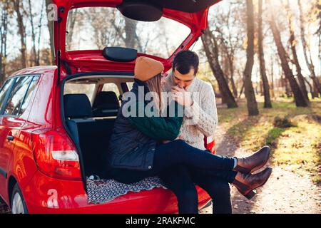 Couple amoureux heureux de se détendre dans le coffre de voiture dans la forêt d'automne. Homme embrassant les mains de la femme. Se déplacer en voiture à l'automne. Banque D'Images