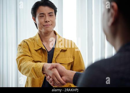 Homme asiatique souriant serrant la main du nouveau membre de l'équipe Banque D'Images