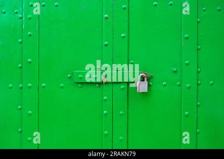 Portes métalliques vertes vibrantes avec grands rivets, verrouillées avec un verrou et un cadenas. Banque D'Images