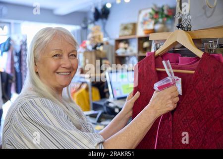 Portrait de la femme bénévole senior travaillant dans la boutique de la Charité ou le magasin Thrift vendant des vêtements d'occasion et durables Banque D'Images