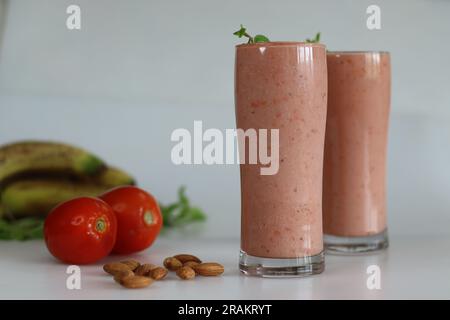 Smoothie tomate banane. Une boisson saine à base de tomates mûres et de bananes congelées dans du lait d'amande servie dans un long verre avec des feuilles de menthe fraîche. Filmé Banque D'Images