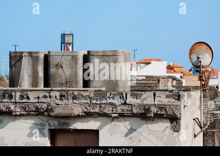 Réservoirs de ciment pour le stockage de l'eau dans une maison délabrée à réformer et manque d'entretien à côté d'une antenne parabolique rouillée. Banque D'Images