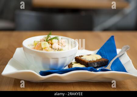 Un bol de soupe finlandaise Lohikeitto servi sur une table en bois avec un morceau de pain de seigle suédois. Bouillon crémeux, pommes de terre tendres et saumon rose feuilleté Banque D'Images