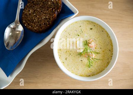 Un bol de soupe finlandaise Lohikeitto servi sur une table en bois avec un morceau de pain de seigle suédois. Bouillon crémeux, pommes de terre tendres et saumon rose feuilleté Banque D'Images