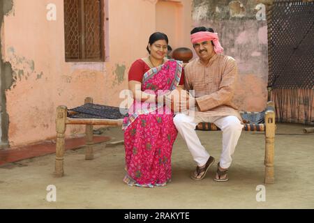 Femmes indiennes rurales heureuses à Saree assis avec son mari tenant la banque de Piggy. Famille aspirative montrant son amour envers leur argent économisé. Banque D'Images