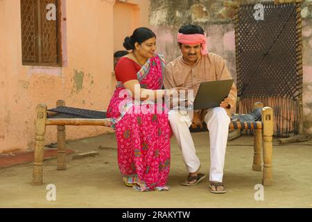 Mari et femme sont heureux de faire le paiement en ligne. Couple indien rural effectuant le paiement par carte de crédit. Couple assis sur un lit dans le couloir. Banque D'Images