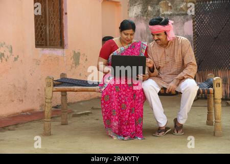 Mari et femme sont heureux de faire le paiement en ligne. Couple indien rural effectuant le paiement par carte de crédit. Couple assis sur un lit dans le couloir. Banque D'Images