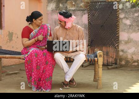 Famille de village indien heureux en utilisant l'ordinateur portable assis à l'extérieur de la maison. Mari et femme sont heureux de faire le paiement en ligne tenant la carte de crédit en main Banque D'Images