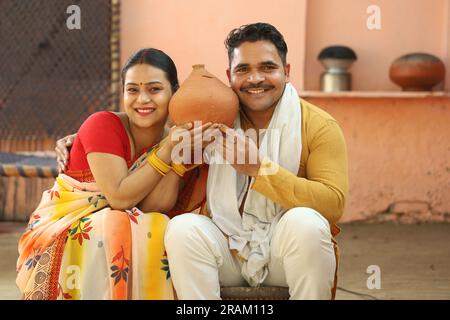 Femmes indiennes rurales heureuses à Saree assis avec son mari tenant Piggy Bank. Famille montrant son amour envers leur argent économisé. Insertion de pièces de monnaie. Banque D'Images