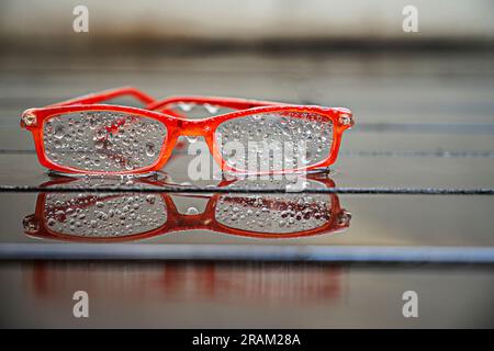 Une paire de verres correcteurs à bordure orange imbibés de gouttelettes d'eau sur un plancher de planche humide Banque D'Images