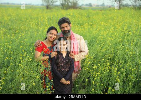 Famille heureuse de fermiers indiens debout dans le champ de moutarde dans la journée profitant des profits agricoles. Ils sont heureux de bénéficier des cultures de moutarde. Banque D'Images