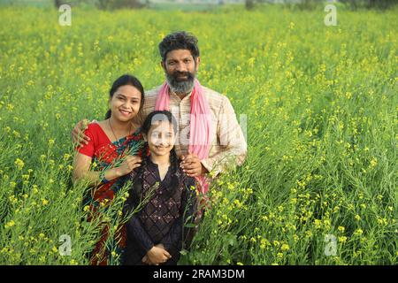 Famille heureuse de fermiers indiens debout dans le champ de moutarde dans la journée profitant des profits agricoles. Ils sont heureux de bénéficier des cultures de moutarde. Banque D'Images