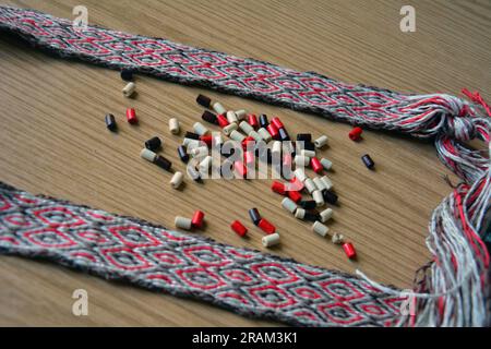 Gros plan d'une ceinture faite à la main produite par tissage de comprimés et quelques perles brunes, beiges et rouges. Image horizontale avec mise au point sélective Banque D'Images