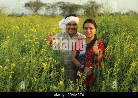 Heureux couple de fermiers indiens debout dans le champ de moutarde appréciant les profits agricoles et heureux de voir les bénéfices des cultures agricoles florissantes. Banque D'Images