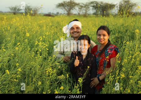 Famille heureuse de fermiers indiens debout dans le champ de moutarde dans la journée profitant des profits agricoles. Ils sont heureux de bénéficier des cultures de moutarde. Banque D'Images