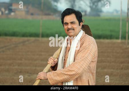 Portrait d'un fermier indien heureux labourant le champ manuellement en une journée. Tenir un outil agricole en main. Pelle et houe à outils de creusement en main. Banque D'Images