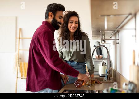 Heureux couple arabe buvant du vin à l'intérieur de la cuisine, homme versant de l'alcool de bouteille dans des verres Banque D'Images