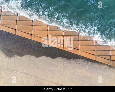 Vue aérienne des vagues se brisant sur les marches bétonnées d'une promenade à marée haute. Banque D'Images