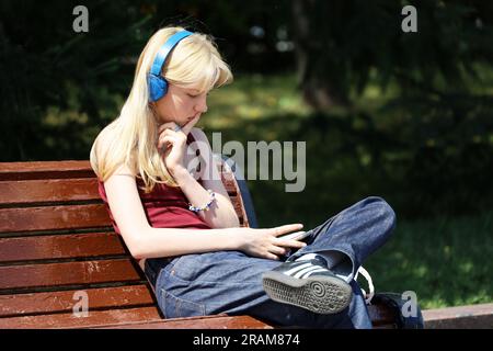 Fille blonde dans les écouteurs assis sur la rue de la ville avec smartphone dans les mains Banque D'Images